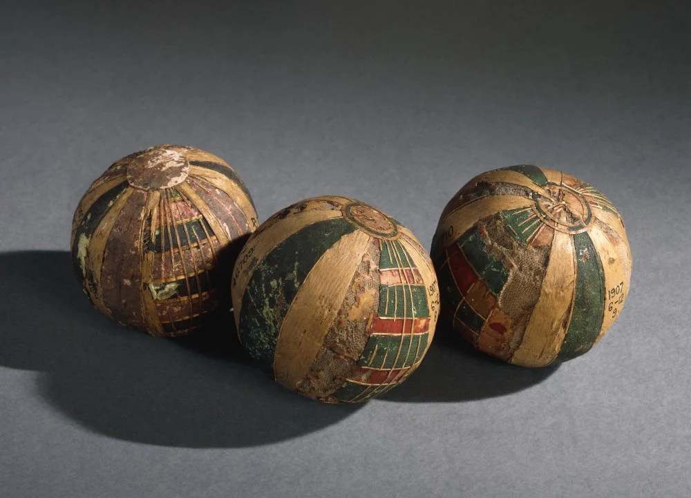 Toy ball made of linen, hollow, exterior elaborated with red and green segmented decoration form by strips of reed, with circular fragments of reed at either end, damaged. Roman Period. Found in Egypt/The Trustees of the British Museum