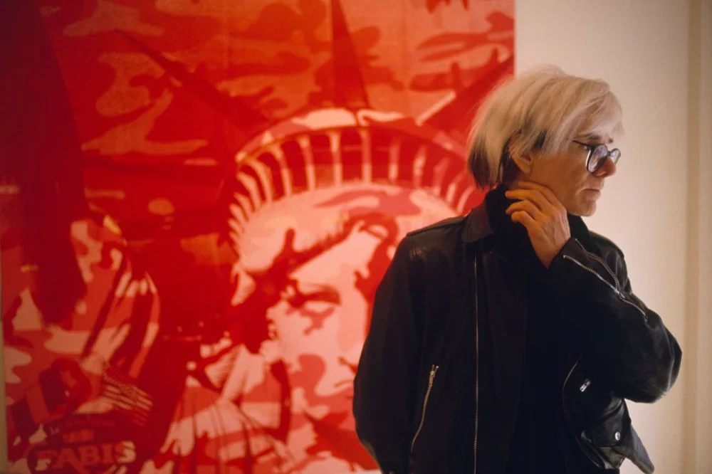 American Painter Andy Warhol, standing in front of a painting, circa 1970/David Lefranc/Kipa/Sygma via Getty Images