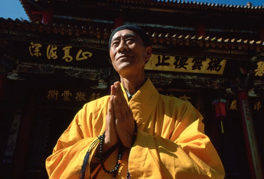   A Buddhist monk in saffron coloured robes with hands together while praying at the Buddhist Temple in Huating, China/Tim Graham/Getty Images