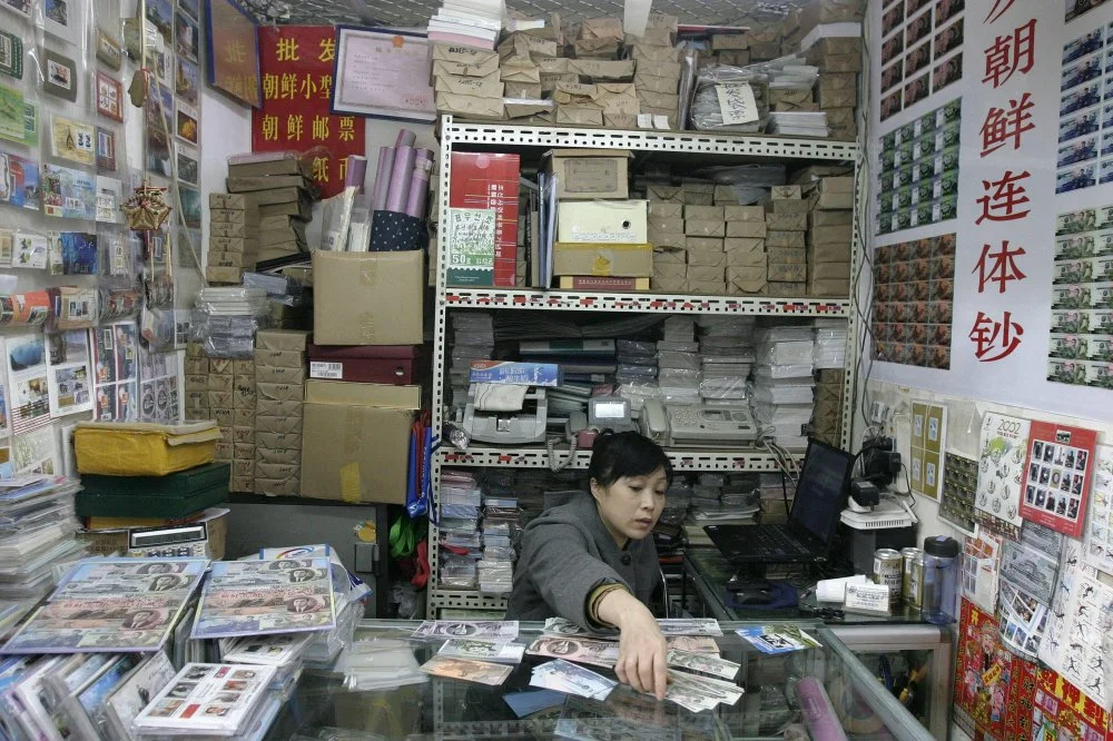 Продавец сортирует памятные банкноты КНДР на рынке марок в Пекине/ imago/Xinhua/Alamy