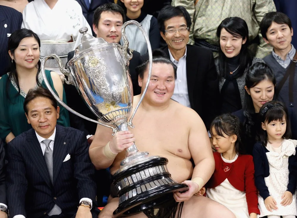 Hakuho Sho picks up a trophy after winning a sumo tournament. 2014/The Asahi Shimbun via Getty Images 
